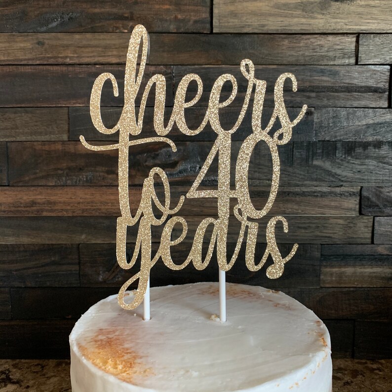 May include: Gold glitter cake topper with the text "Cheers to 40 years" on a white cake.