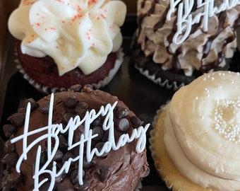 May include: Four cupcakes with white frosting and chocolate frosting. Each cupcake has a white plastic topper that says "Happy Birthday".