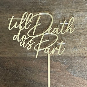 May include: Gold acrylic cake topper with the text "till death do us part" in a cursive font.