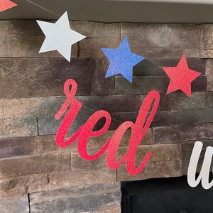 May include: A patriotic banner with red glitter text that reads "red" and white glitter text that reads "white". The banner also features glittery stars in red, white, and blue, perfect for a 4th of July celebration.