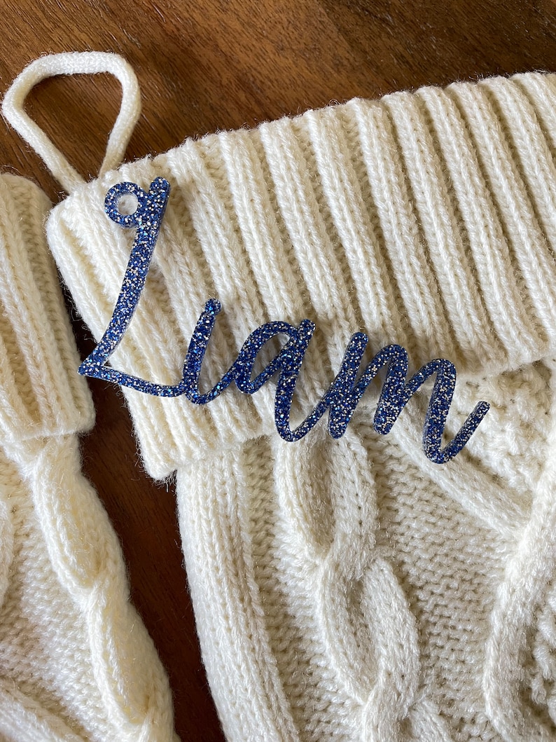 May include: White knitted stocking with a blue glitter name tag that says "Liam".