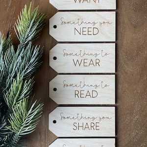 May include: Six wooden gift tags with a string attached. Each tag has a different phrase written on it: "Something you WANT", "Something you NEED", "Something to WEAR", "Something to READ", "Something you SHARE", and "Something to DO".