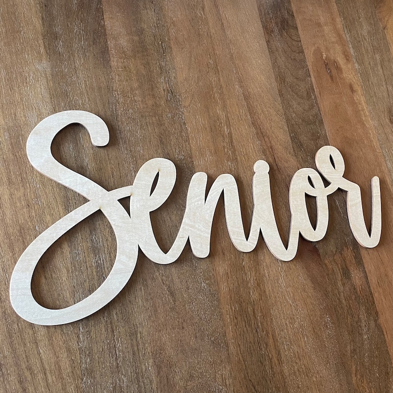 May include: A white wooden sign with the word "Senior" written in a cursive font.