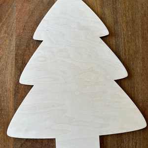 May include: A wooden Christmas tree cutout with a natural wood grain finish. The tree has a classic shape with three tiers and a rectangular base. The unfinished wood allows for customization with paint, stain, or other decorative elements.