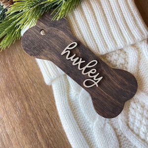 May include: White knitted stocking with a brown wooden bone-shaped tag that says "huxley" in cursive.
