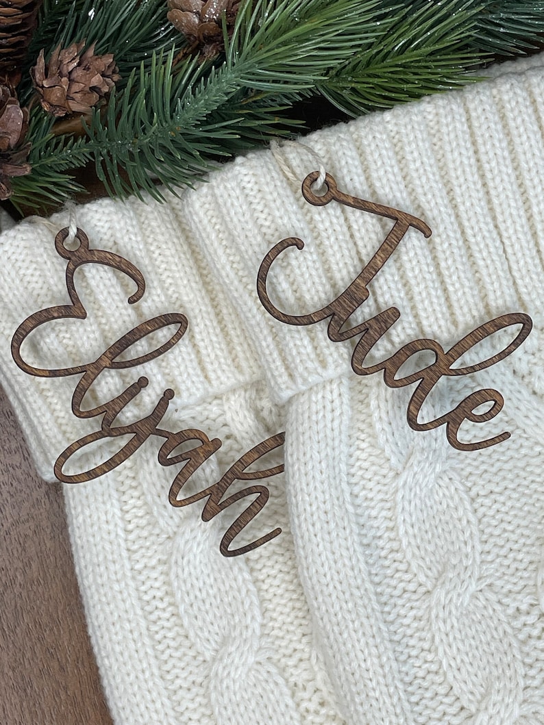 May include: Two wooden Christmas stocking ornaments with the names "Elyzah" and "Jude" written in cursive.