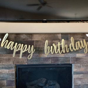 May include: A gold glitter "happy birthday" banner with white bunny cutouts on each end. The banner is strung across a stone fireplace, creating a festive and celebratory atmosphere. Perfect for a birthday party.