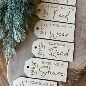 May include: Six wooden gift tags with the name "Paige" and the words "Something You Want", "Something You Need", "Something To Wear", "Something To Read", "Something To Share", and "Something To Do" written in cursive.