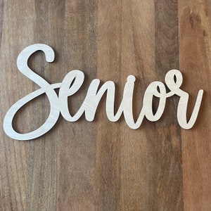 May include: White wooden sign with the word "Senior" written in a cursive font.