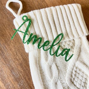 May include: White knitted Christmas stocking with a green glitter name tag that says "Amelia" on it.