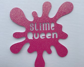 May include: Pink glitter slime splatter cake topper with the words "slime queen" cut out in the center.