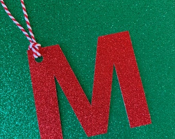 May include: Red glitter letter M with a white and red string attached to the top.