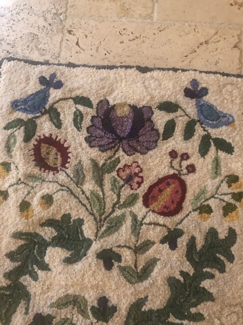 May include: A white rug with a floral design featuring purple, red, yellow, and green flowers. Two blue birds are on either side of the rug.