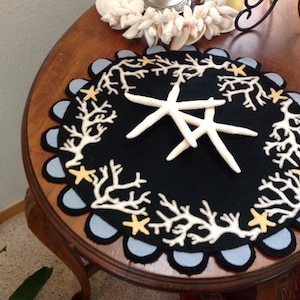 May include: A round black felt rug with a white coral design and a blue scalloped edge.  The rug has yellow starfish accents and features three white starfish in the center.