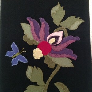 May include: A black felt wall hanging with a purple, pink, and red flower with green leaves and a blue butterfly.