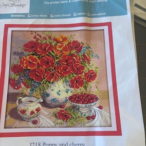 May include: A cross-stitch kit featuring a floral still life with red poppies and cherries. The kit includes pre-printed fabric, cotton thread, a needle, and instructions. The text "Joy Sunday Cross Stitch" and "J218 Poppy and cherry" are visible.