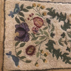 May include: A cream-colored rug with a floral design featuring blue birds, green leaves, and pink, purple, and yellow flowers.