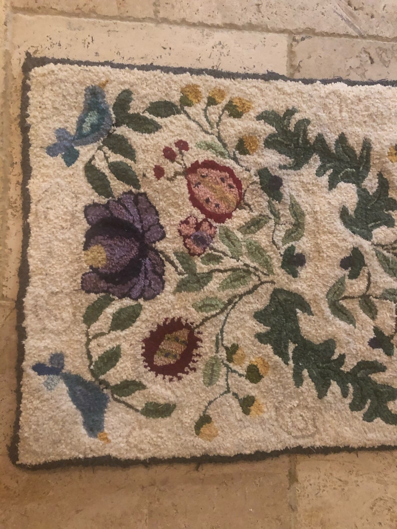 May include: A cream-colored rug with a floral design featuring blue birds, green leaves, and pink, purple, and yellow flowers.