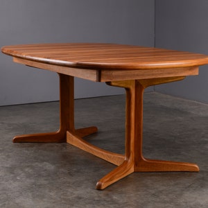 May include: A rectangular wooden dining table with rounded edges and a smooth, warm-toned grain. The table features a central support structure with two vertical pillars connected by a horizontal base, each ending in two splayed feet.