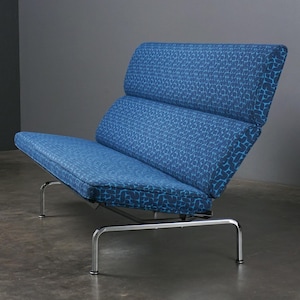 May include: A modern blue lounge chair with a patterned design. The chair features a low profile with a seat and backrest made of a blue fabric with a repeating pattern. The frame is made of polished metal.