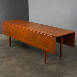 May include: A rectangular wooden drop-leaf table with a warm brown finish. The table features a smooth, flat top surface and two hinged side leaves that hang vertically. It is supported by four cylindrical wooden legs positioned at the corners.