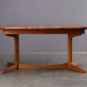 May include: A rectangular wooden dining table with rounded edges and a smooth, polished finish. The table features a central support structure with two vertical legs connected by a curved horizontal base piece that extends into four feet.