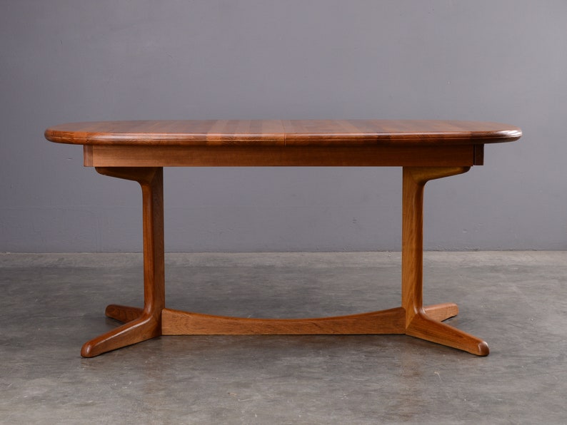 May include: A rectangular wooden dining table with rounded edges and a smooth, polished finish. The table features a central support structure with two vertical legs connected by a curved horizontal base piece that extends into four feet.