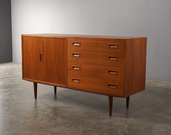 Könnte beinhalten: Ein Sideboard im Mid-Century-Modern-Stil aus Holz mit warmem, rötlich-braunem Finish. Es hat eine Schranktür auf der linken Seite und vier Schubladen auf der rechten Seite, alle mit eingelassenen Griffen. Das Sideboard steht auf vier konischen Beinen.