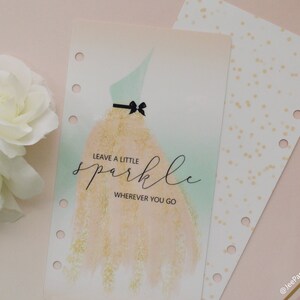 Pode incluir: Uma inser&ccedil;&atilde;o de planejador com uma ilustra&ccedil;&atilde;o em aquarela de um vestido, com um corpete verde-menta e uma saia dourada. O texto "LEAVE A LITTLE sparkle WHEREVER YOU GO" est&aacute; escrito em it&aacute;lico. Uma segunda inser&ccedil;&atilde;o com pontos dourados &eacute; vis&iacute;vel.