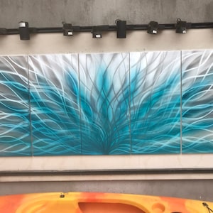 May include: A four-panel metal wall art piece with a blue and silver abstract design. The artwork features a swirling pattern of lines that create a sense of movement and energy.