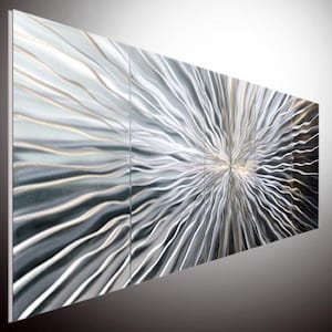 May include: A large abstract metal wall sculpture with a silver and gray finish. The sculpture is made up of multiple panels that are joined together to create a flowing, wave-like pattern.