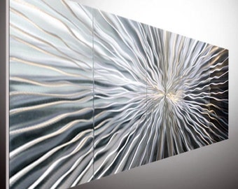 May include: A large abstract metal wall sculpture with a silver and grey finish. The sculpture is made up of multiple panels that are joined together to create a flowing, wave-like pattern.