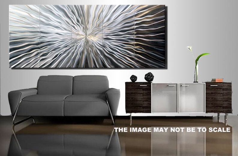 May include: A large abstract metal wall art piece with a silver and gray color scheme. The art is made up of multiple panels and features a swirling, wave-like pattern. The art is displayed on a wall above a gray sofa and a wooden cabinet with glass doors.
