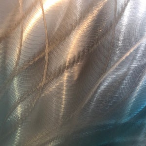 May include: A close-up of a brushed metal surface with a swirling pattern. The metal has a silvery-grey color with a hint of blue.