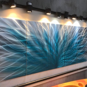 May include: A modern abstract metal wall art sculpture with a blue and silver color scheme. The sculpture is made up of four panels and features a swirling, organic design.