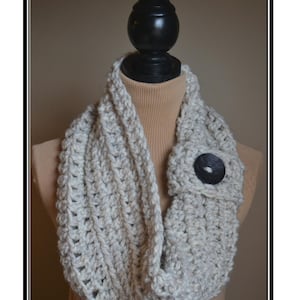 May include: A crocheted cowl in a light gray color with a black button. The cowl is displayed on a mannequin. The text "Yorkshire Button Cowl Pattern" is at the bottom of the image.