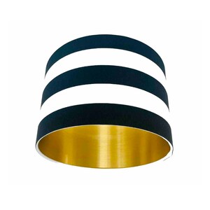 May include: A black and white striped lampshade with a gold interior. The lampshade has three white stripes.