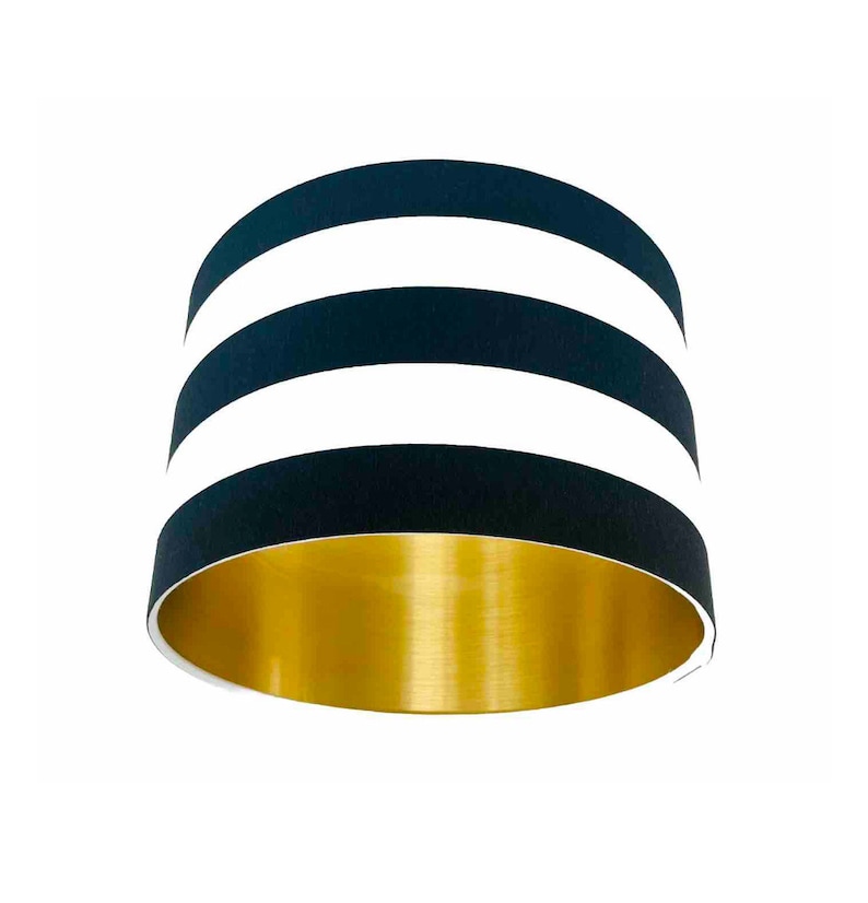 May include: A black and white striped lampshade with a gold interior. The lampshade has three white stripes.