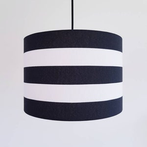 May include: Black and white striped pendant lampshade. The lampshade is cylindrical and has three white stripes.