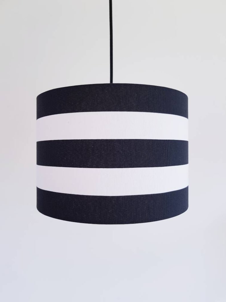 May include: Black and white striped pendant lampshade. The lampshade is cylindrical and has three white stripes.