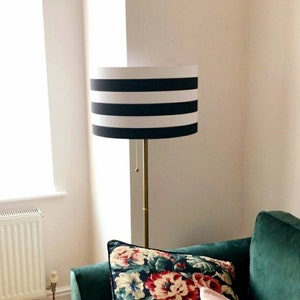 May include: A black and white striped lampshade with a gold metal base. The lamp is sitting on a green sofa with floral patterned pillows.