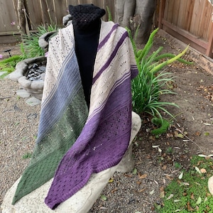 May include: A triangular shawl with a multi-colored striped pattern in shades of beige, blue, green, and purple. The shawl is made of a delicate, lacy yarn and has a fringed edge.