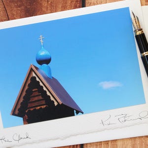 May include: A photograph of a church with a blue dome and cross, a black fountain pen, and a decorative candle with gold accents. The image is on a wooden surface.