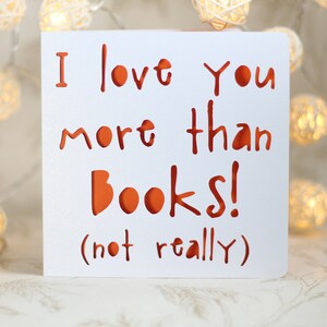 May include: White card with the text "I love you more than books! (not really)" in red lettering.