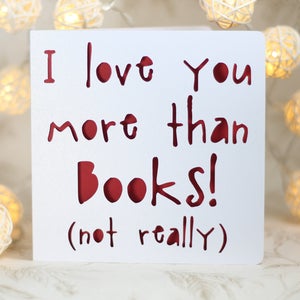 May include: White card with red lettering that reads "I love you more than books! (not really)"