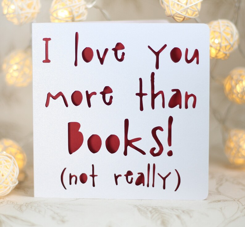 May include: White card with red lettering that reads "I love you more than books! (not really)"