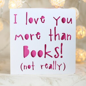 May include: White card with pink lettering that reads "I love you more than books! (not really)"