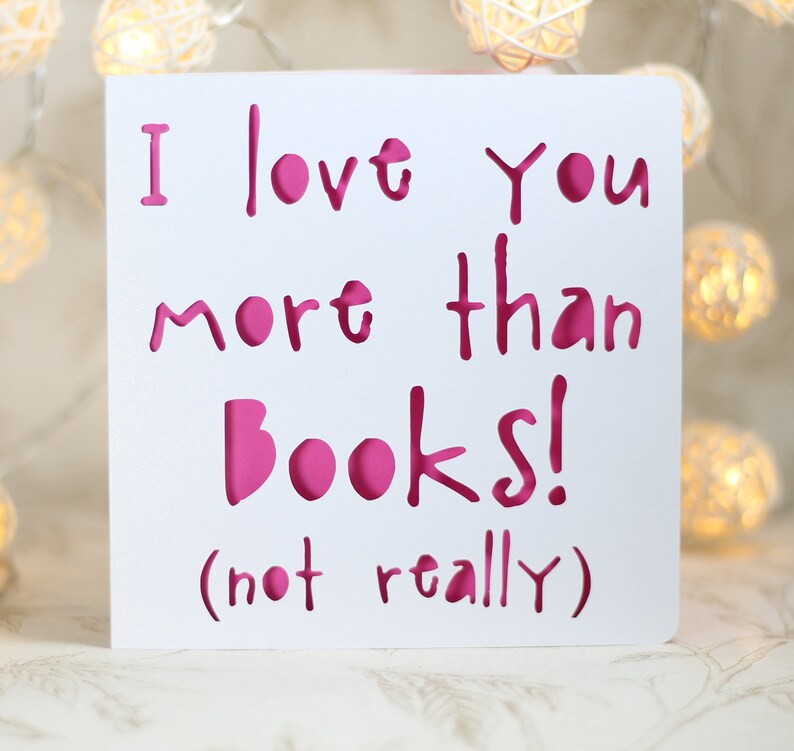 May include: White card with pink lettering that reads "I love you more than books! (not really)"
