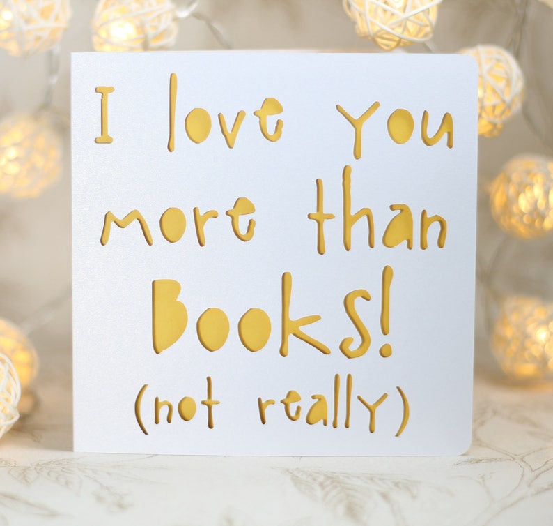 May include: White card with the text "I love you more than books! (not really)" in gold lettering.