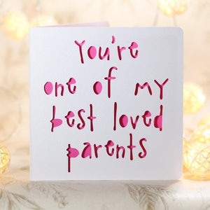 May include: White card with the words "You're one of my best loved parents" written in pink. The words are cut out of the card, creating a layered effect.
